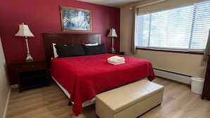 A bedroom with a bed, a bench, a nightstand, a lamp, a picture on the wall, and a window with blinds. - Meadow Drive Home In Beautiful Lake Tahoe Nevada (Stateline)