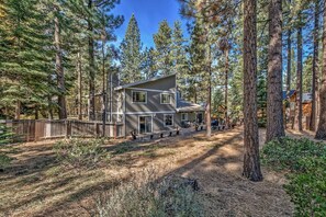 A two-story cabin with a deck, surrounded by tall pine trees.