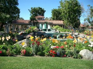 A garden with a fountain, colorful flowers, and a building with a tiled roof.