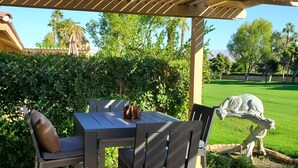 An outdoor patio with a wooden pergola, a table with chairs, and a statue of a llama. - Green Vistas on the Tenth Tee is a one story end unit with wall to wall windows  (Palm Desert)