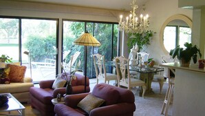 A living room with a sofa, chairs, a dining table, and a chandelier. - Green Vistas on the Tenth Tee is a one story end unit with wall to wall windows  (Palm Desert)