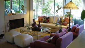 A modern living room with a sofa, ottoman, and coffee table. There is a fireplace, large windows, and a lamp. - Green Vistas on the Tenth Tee is a one story end unit with wall to wall windows  (Palm Desert)