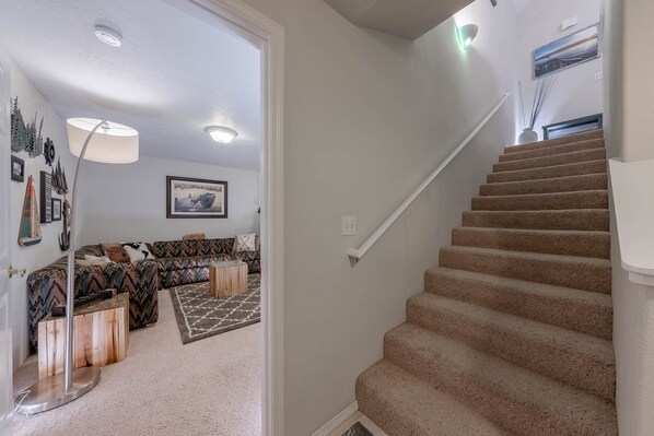 Un escalier menant à l’étage supérieur, un salon avec un canapé à motifs, une table d’appoint en bois et un lampadaire.