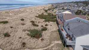 A coastal property with a beach view, a covered deck with outdoor seating, and a large house with a garage.