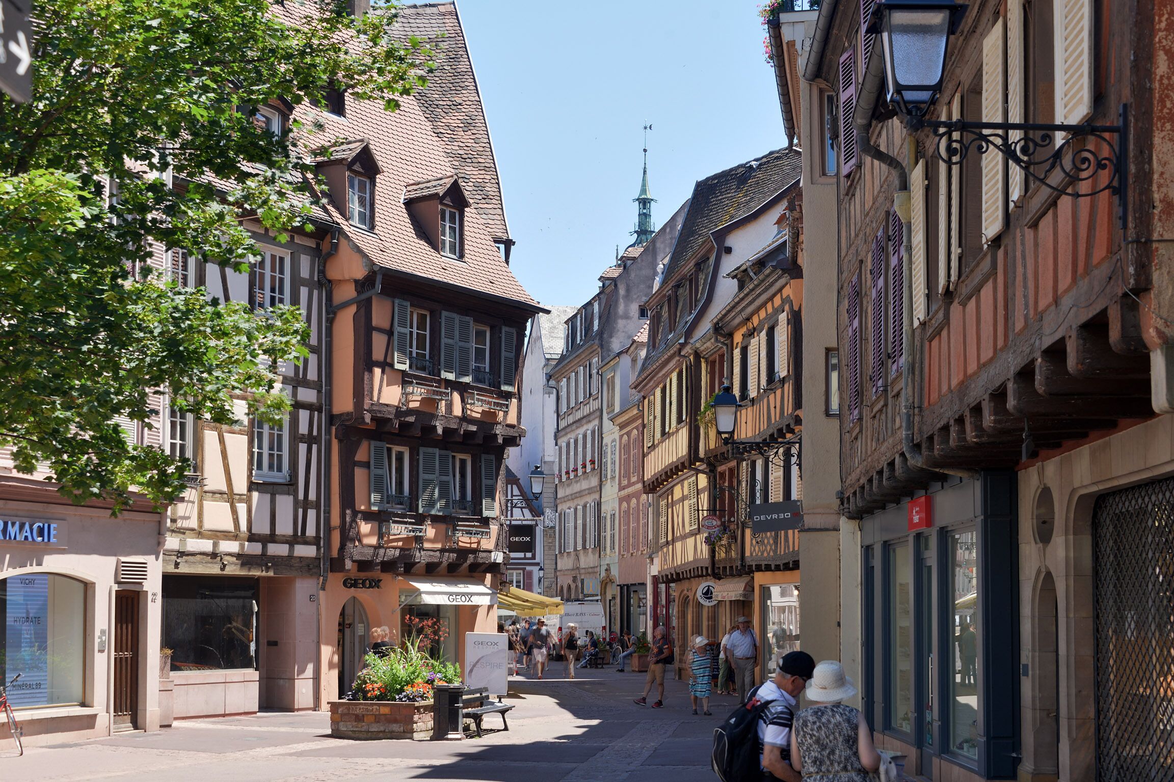 A narrow street lined with traditional half-timbered buildings, some with visible ground-floor shops and signage.