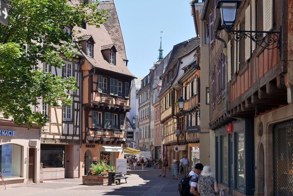 A narrow street lined with traditional half-timbered buildings, some with visible ground-floor shops and signage.
