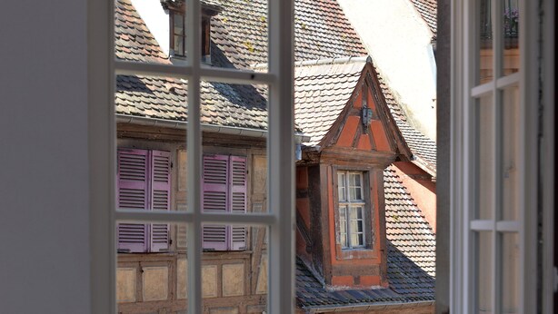 A view through a window of a building with traditional architecture, featuring multiple windows and a pitched roof. - Upscale apartment in the heart of the historic center of Colmar (Colmar)