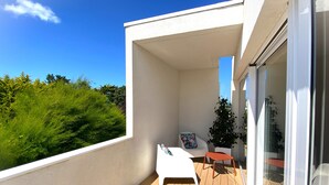 Un balcon avec un plancher en bois, une chaise blanche, une petite table et une plante en pot.