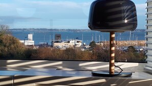 Une lampe moderne posée sur une table, avec vue sur une marina et les bâtiments situés de l’autre côté de l’eau.