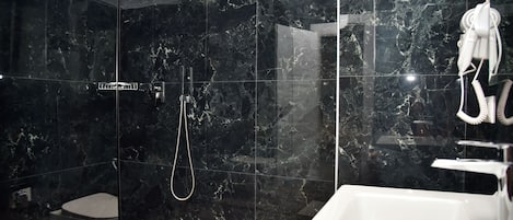 A modern bathroom with a glass-enclosed shower, a white sink, and a marble-tiled wall.