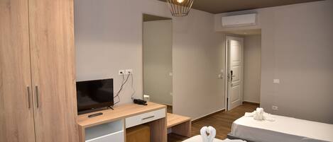 A modern hotel room with a wooden wardrobe, a desk with a flat-screen TV, a mirror, and two beds.