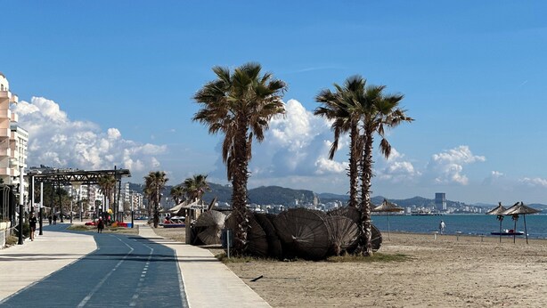 A coastal road with palm trees, a beach, and a cityscape in the background. - Dolanit Hotels Lubjana (Durrës)