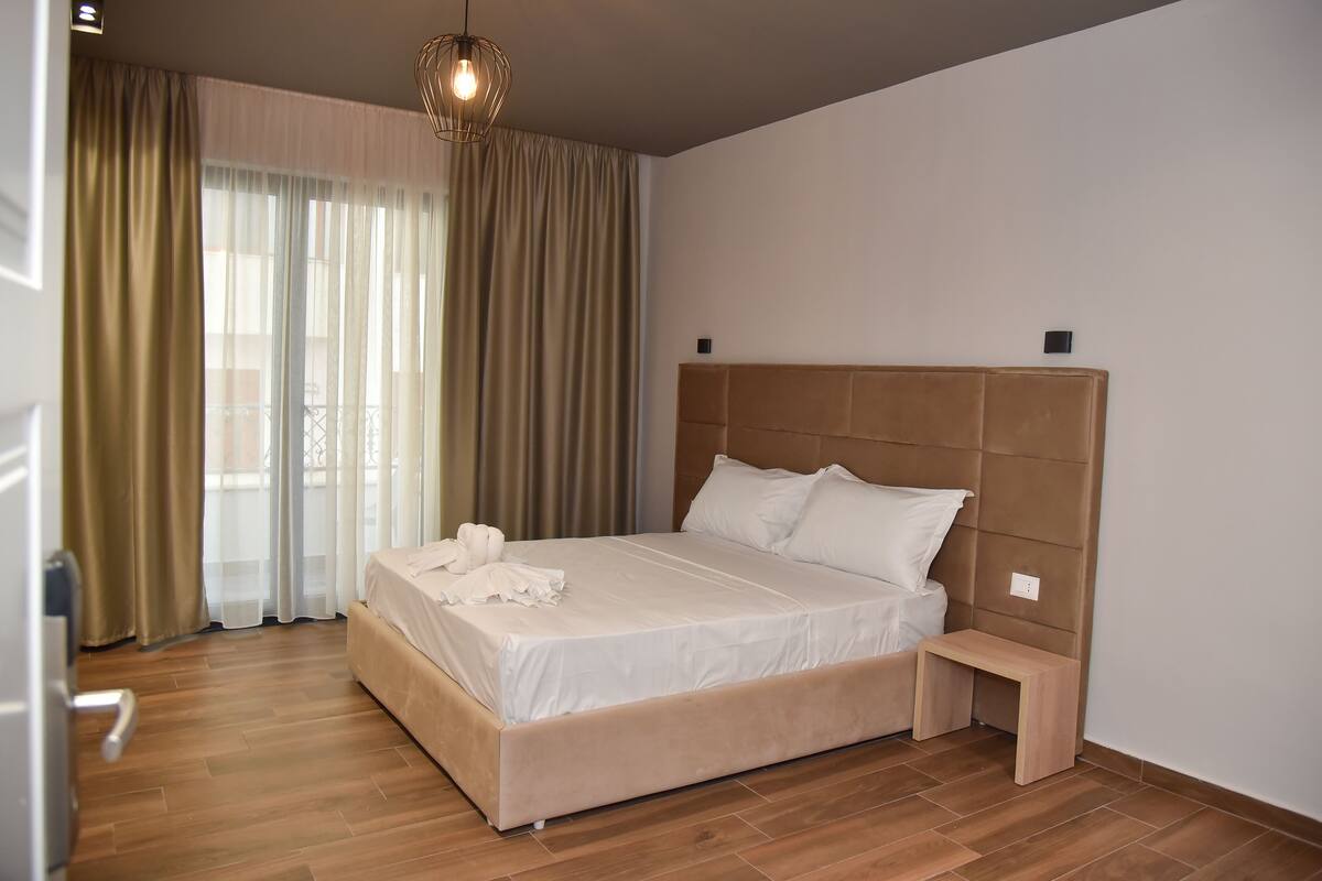 A neatly made bed with a headboard, a bedside table, and a hanging light fixture in a hotel room.