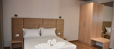 A modern hotel room with a large bed, wooden headboard, and a wardrobe.
