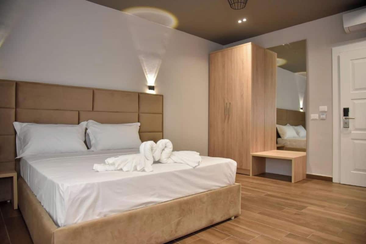 A modern hotel room with a large bed, a wooden wardrobe, a bedside table, and a mirror.