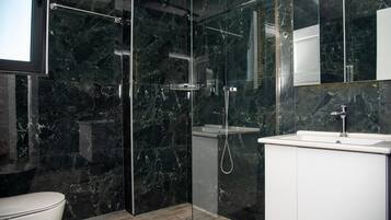 Ein modernes Badezimmer mit einer gläsernen Duschkabine, einem weißen Waschbecken und einer Wand mit Marmorfliesen.
