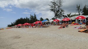 A beach with people sunbathing and swimming, surrounded by red umbrellas. - Beautiful T2 apartment Clear view between sea and mountain near the lagoon (La Saline-Les-Bains)