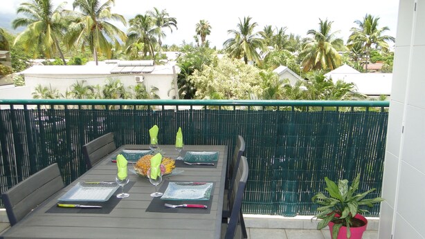 A balcony with a table set for four, a green fence, and a potted plant. - Beautiful T2 apartment Clear view between sea and mountain near the lagoon (La Saline-Les-Bains)