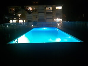 A swimming pool at night with a building in the background.
