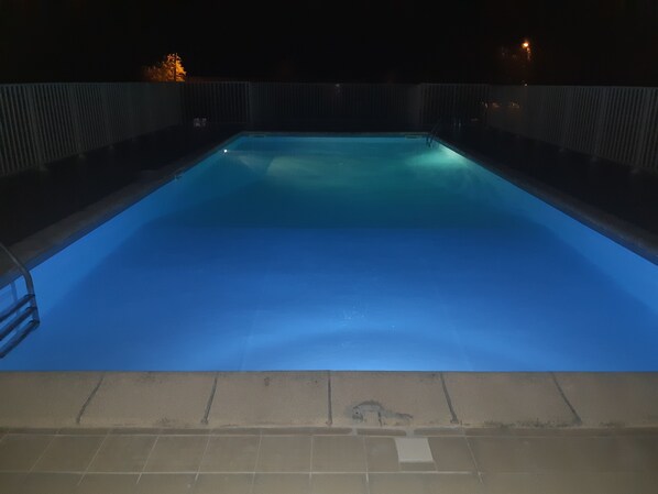 A rectangular swimming pool with a blue tint, surrounded by a metal fence, and a tiled floor leading to the pool.