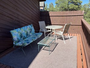 Une terrasse avec un canapé bleu à motifs, deux chaises blanches, une petite table ronde et une chaise en métal.