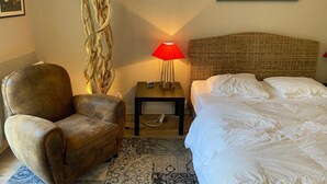 Quarto de hotel com cama, poltrona, mesa de cabeceira com abajur, quadro na parede e objeto decorativo.