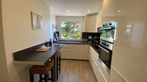 Cozinha compacta com área de refeições, eletrodomésticos embutidos e janela com vista para o verde.