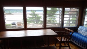 A room with a wooden table and bench, a blue sofa, and large windows with a view of the outdoors.