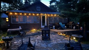 A rustic cabin with a stone patio, outdoor seating, and a barbecue area.