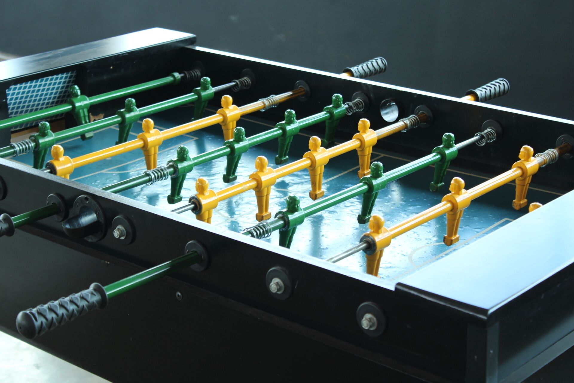 A foosball table with green and yellow figures, black rods, and a blue playing surface.