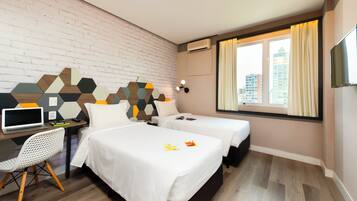 Habitación de hotel con dos camas, un escritorio con una computadora portátil, una silla y vistas a edificios a través de la ventana.