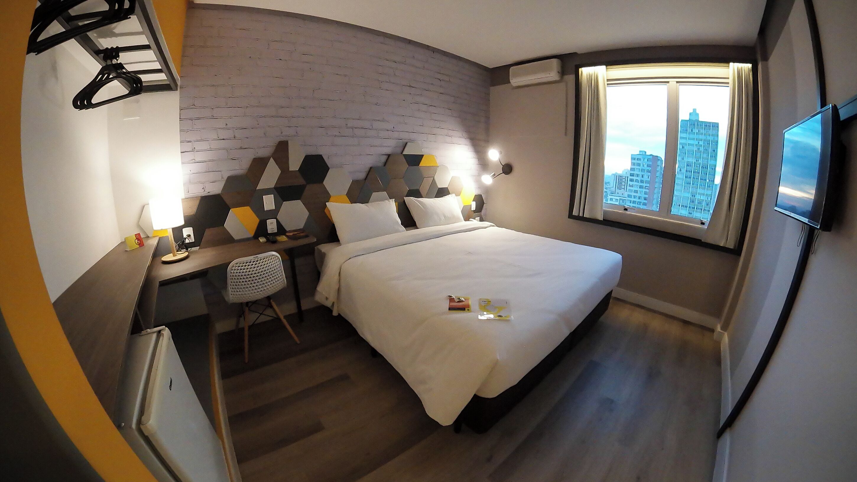 A hotel room with a bed, a desk, a chair, a TV, and a window with a city view.