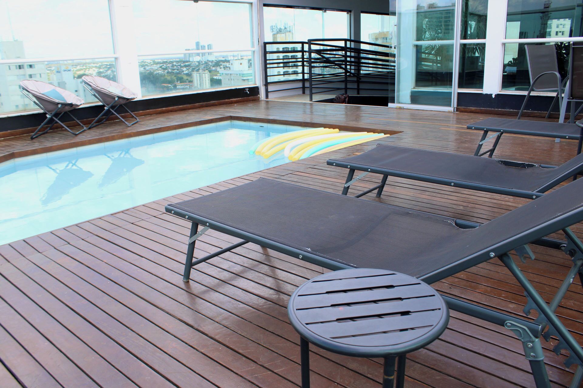 A rooftop pool area with lounge chairs and a small table.