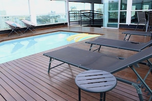 Un área de piscina en la azotea con sillones de descanso y una pequeña mesa.