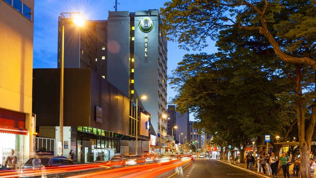 A B&B hotel with a prominent sign, a street with moving traffic, and trees lining the sidewalk. - B&B Hotels Uberlândia (Uberlandia)