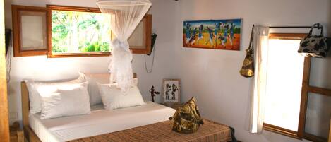 A bedroom with a bed, a canopy, a painting, and a window with curtains.