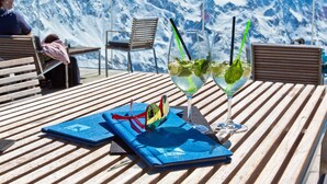 Eine Holzterrasse mit zwei Gläsern Minzgetränk, einem blauen Notizbuch und einer farbenfrohen Tasche.