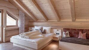 Ein Schlafzimmer mit Holzboden, einem Bett mit Kissen, einem Nachttisch und einer Couch mit Polstern.