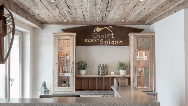 Ein Empfangsbereich mit Holzboden, einem Schild mit der Aufschrift 'Chalet Resort Sölden' und Holzschränken mit Glastüren, die Gegenstände präsentieren.