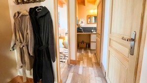 A hallway with wooden flooring, a coat rack with robes, a small kitchenette, and a mirror above the sink. - Gîte dans les bois - Nordic SPA & Nature (Montdurausse)