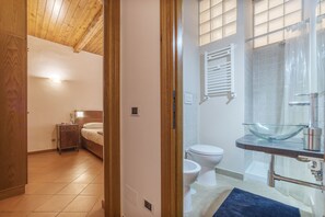 Un baño con lavamanos de vidrio, ducha e inodoro.