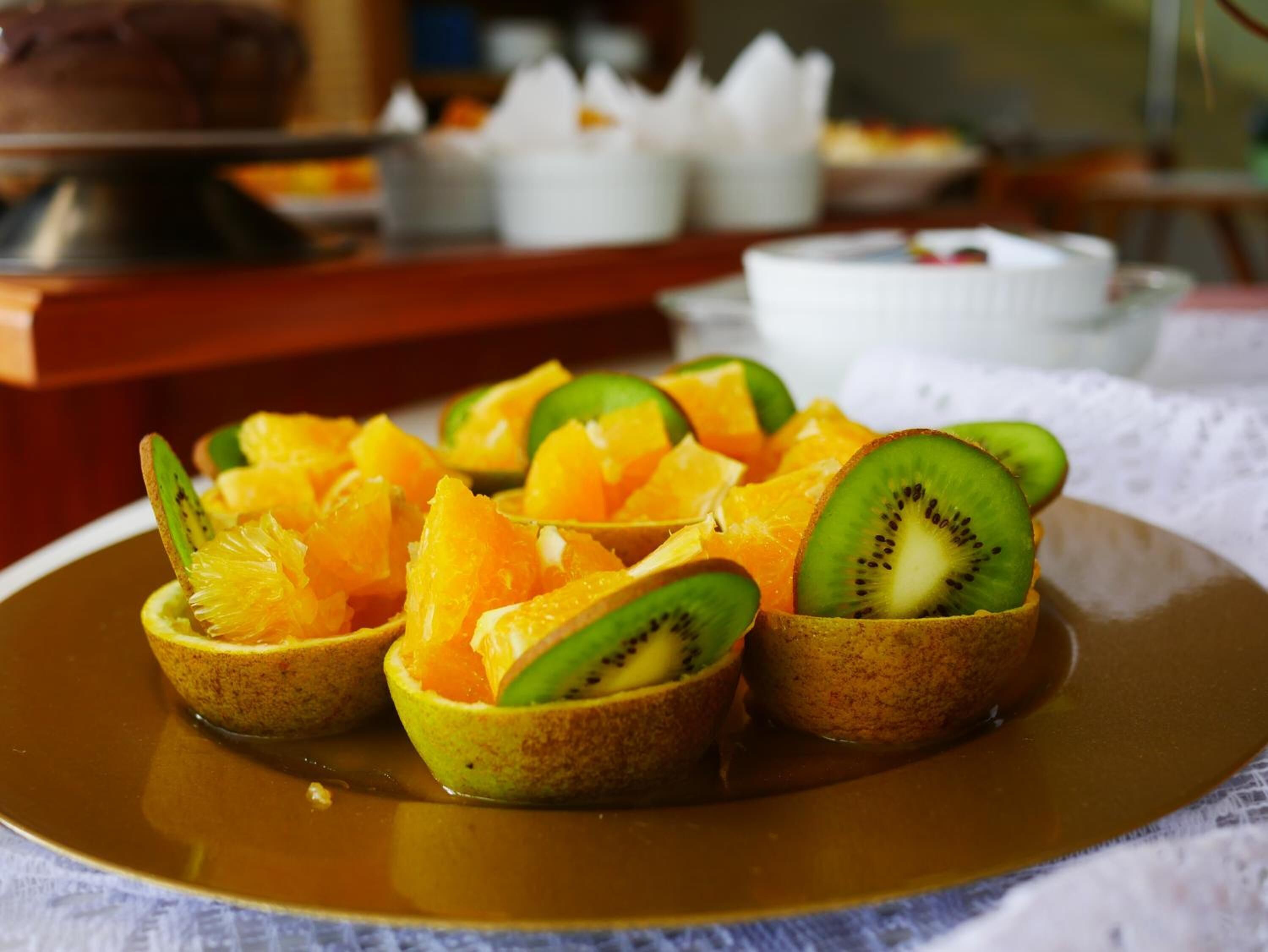 Une assiette de tartelettes aux fruits, garnies de tranches de kiwi et d’orange, est posée sur une table.