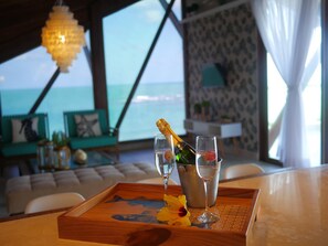 Une chambre avec vue sur la mer, un plateau en bois avec des verres et une bouteille, et une fleur.