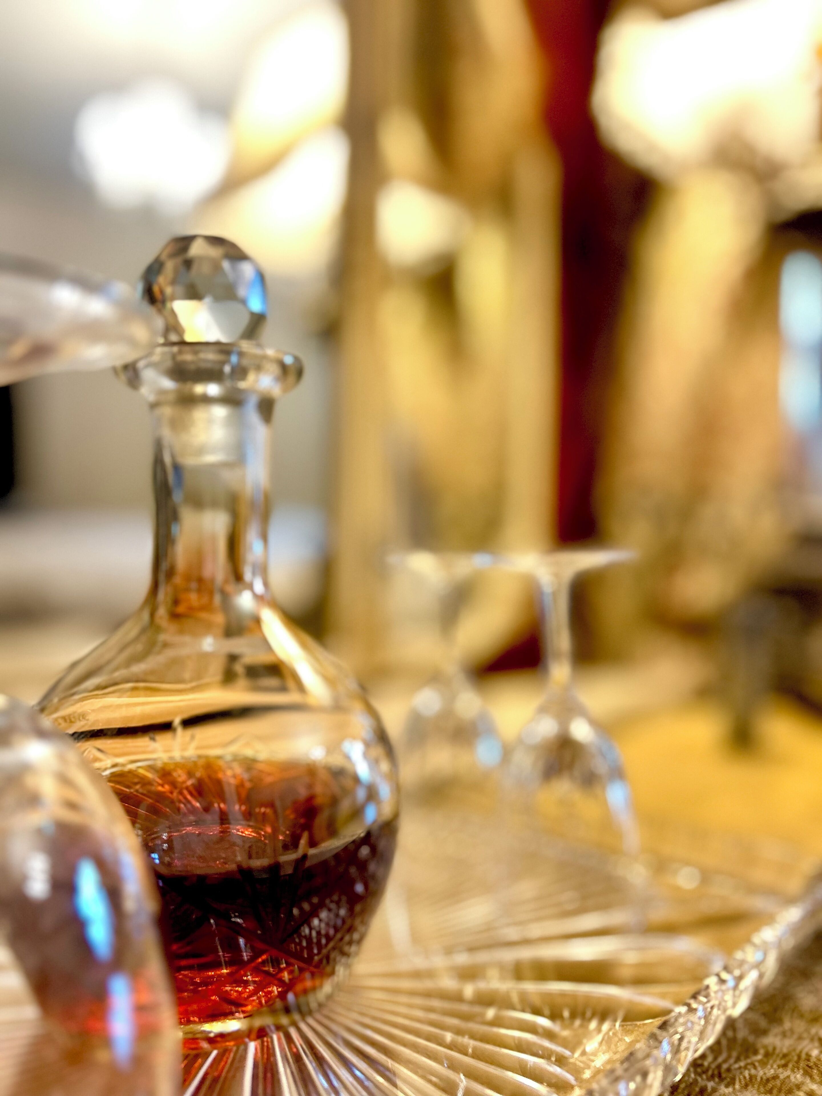 A close-up of a glass decanter with a red liquid, surrounded by other glassware on a table.