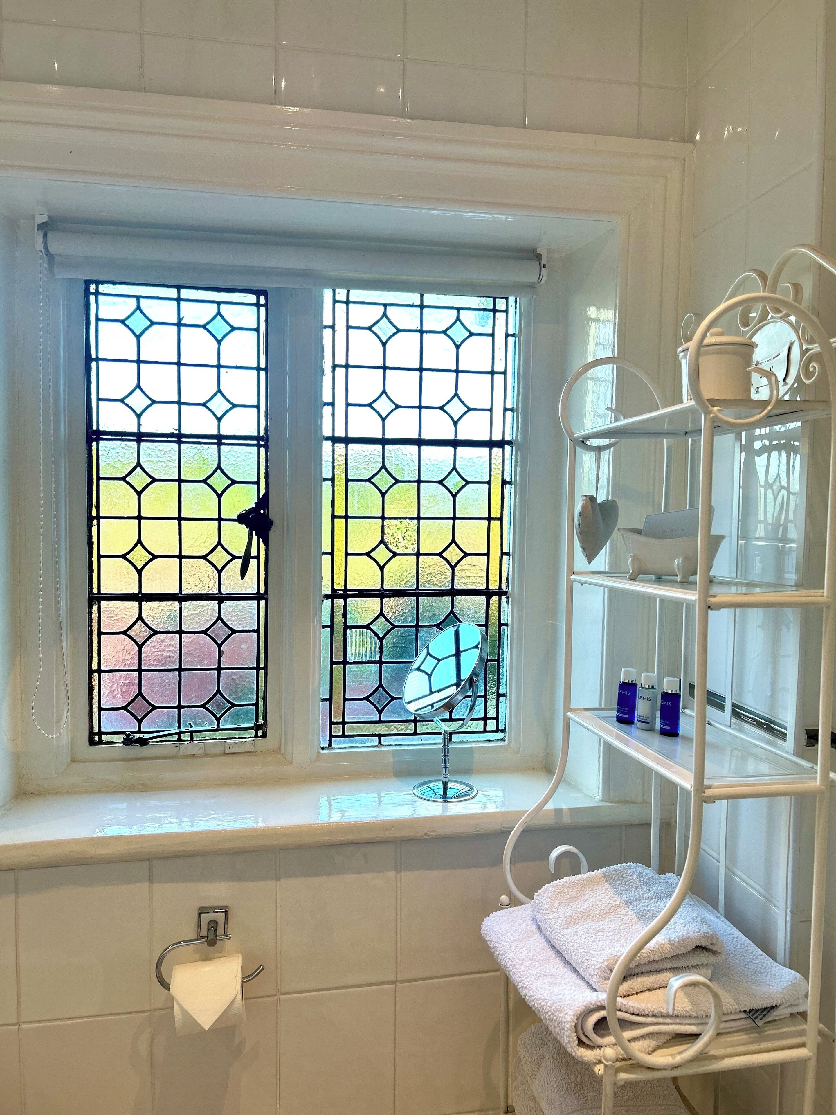 A bathroom with a window, a towel rack, and a shelf with toiletries.