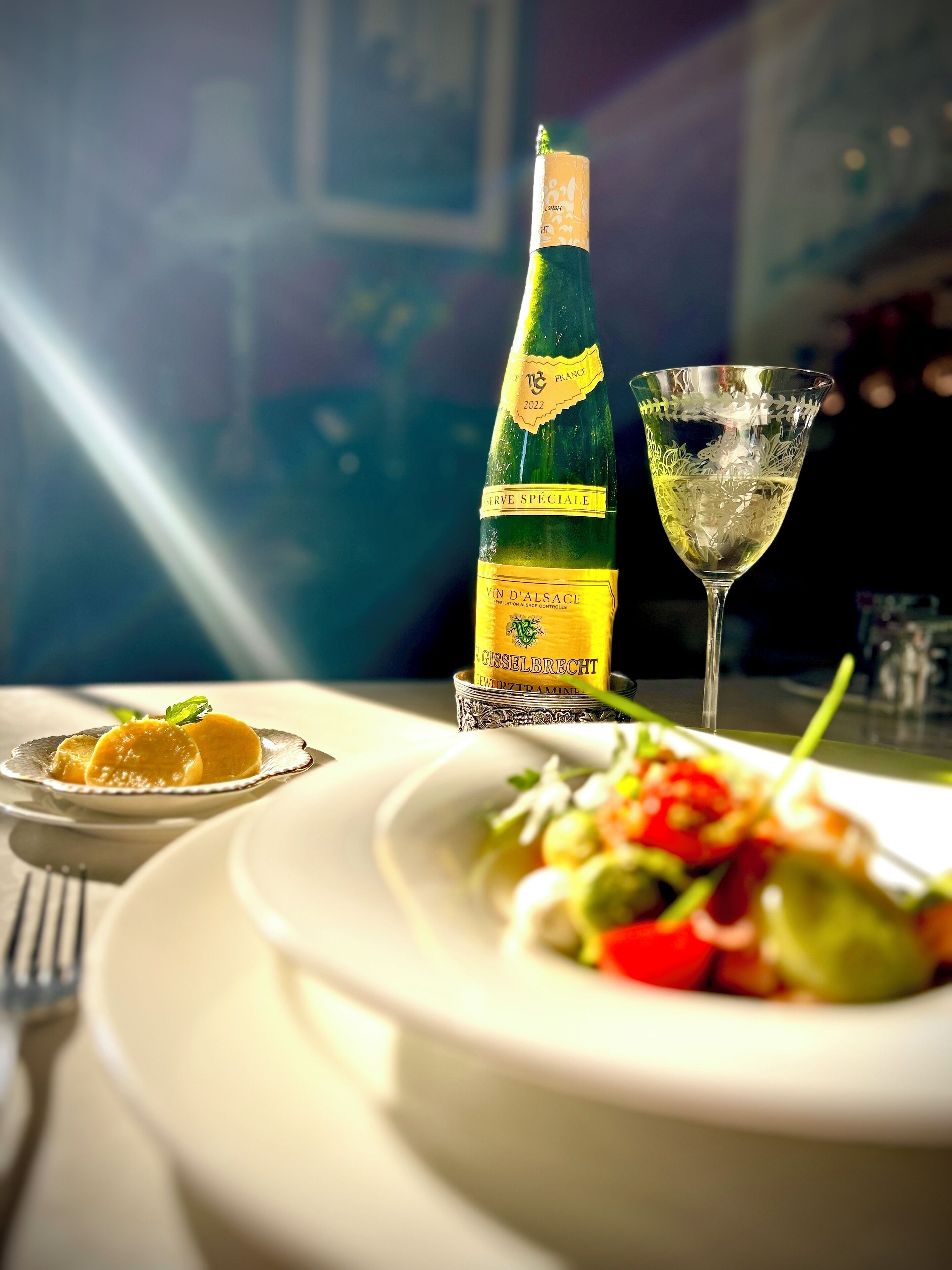 A bottle of wine, a glass of wine, and two plates of food on a table.