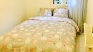 Une petite chambre avec un lit, une fenêtre avec un rideau et un radiateur.
