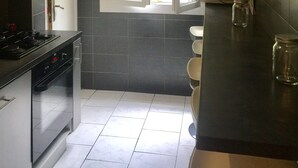 Une cuisine équipée d’une cuisinière à gaz, d’une fenêtre donnant sur un espace verdoyant et d’une machine à café posée sur le plan de travail.