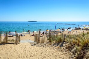 En sandstrand med et træhegn, parasoller og mennesker, der nyder vandet.