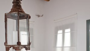 Ein Zimmer mit Holzboden, einem Fenster mit grünem Rahmen, einem runden Tisch, einer Couch mit Kissen und einer hängenden Laterne.